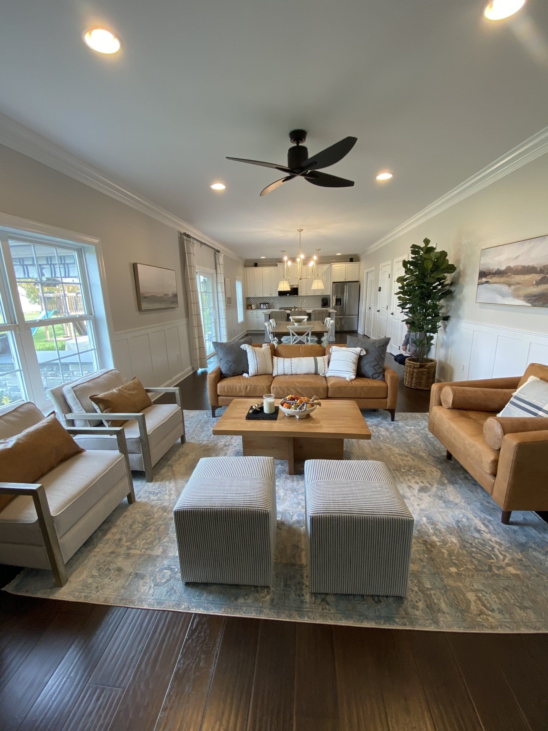 Bright modern living room with gray seating, tan chairs, wood table, and open kitchen in the background