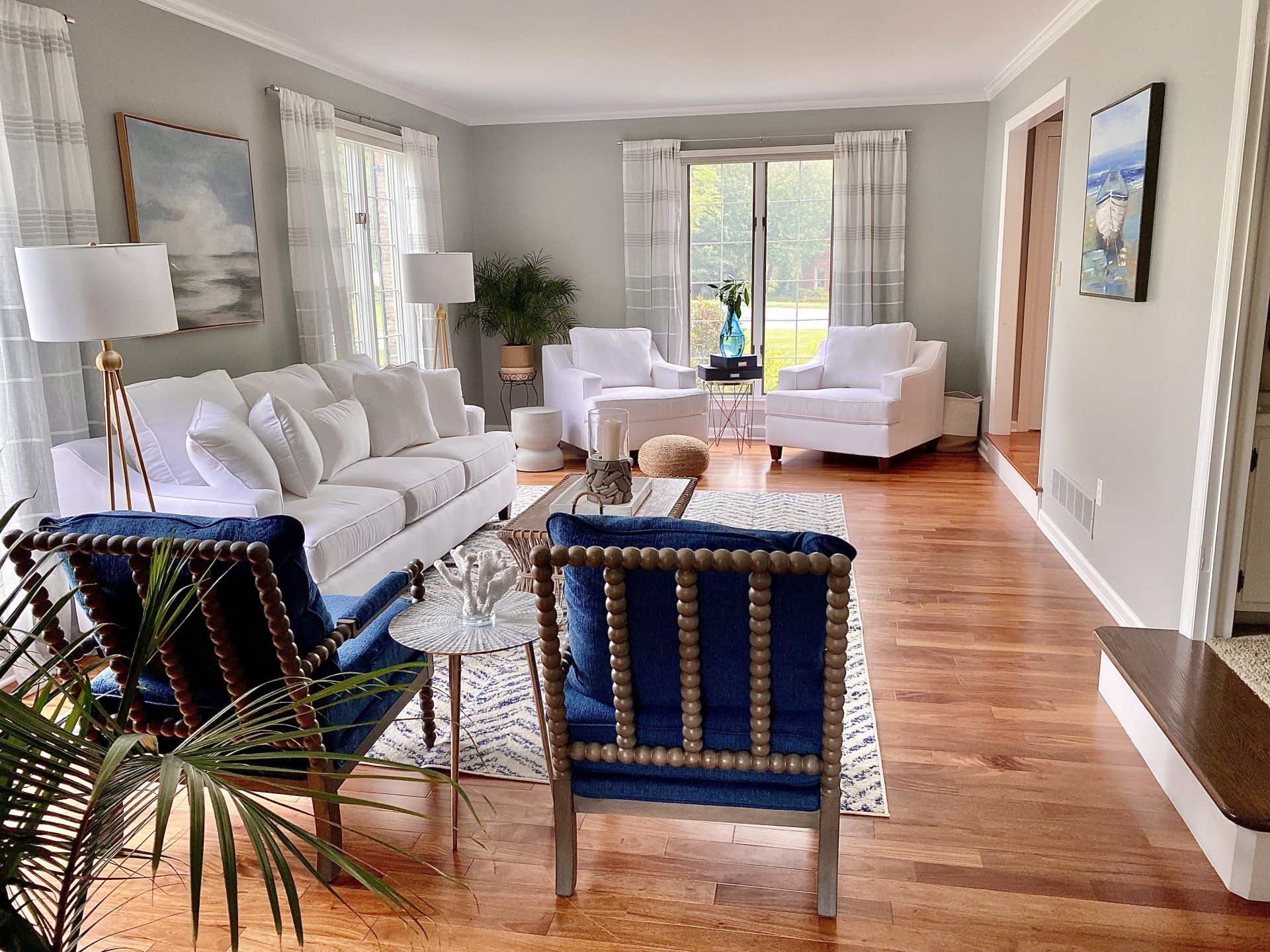 Bright living room with white sofas, blue chairs, hardwood floors, and large windows.