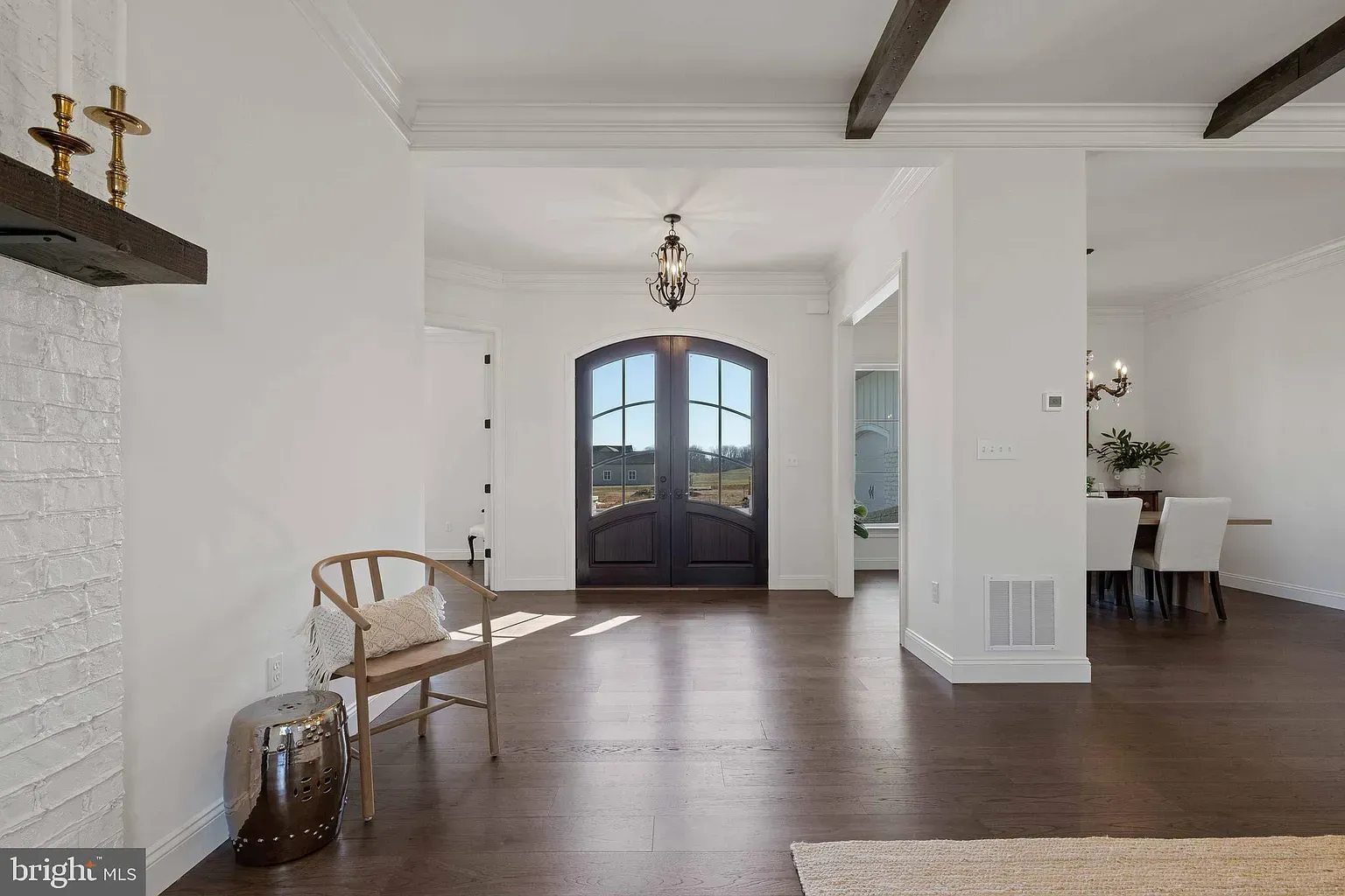 Bright white foyer with dark wood floors, double front doors, a chair, and a dining area in the background
