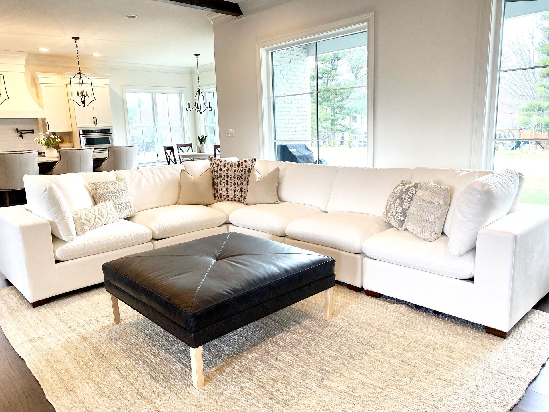 Bright living room with white sectional sofa, black ottoman, and large window over a light rug