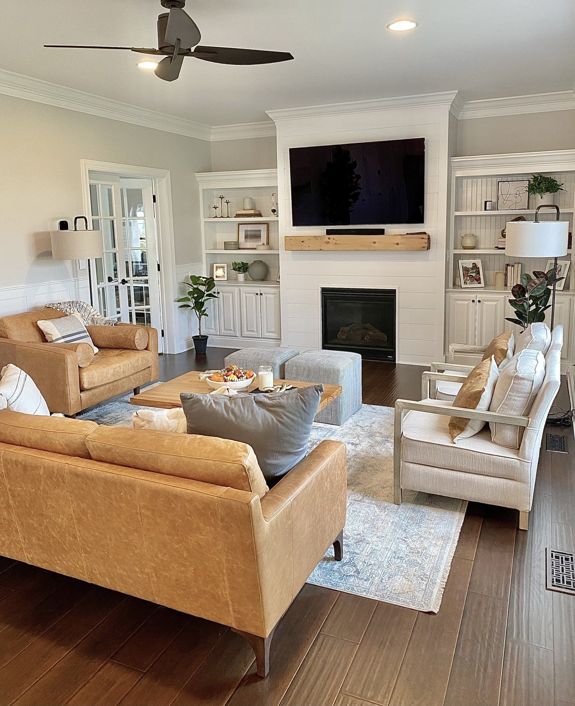 Bright living room with tan and cream chairs, fireplace, wall-mounted TV, and dark wood floor.