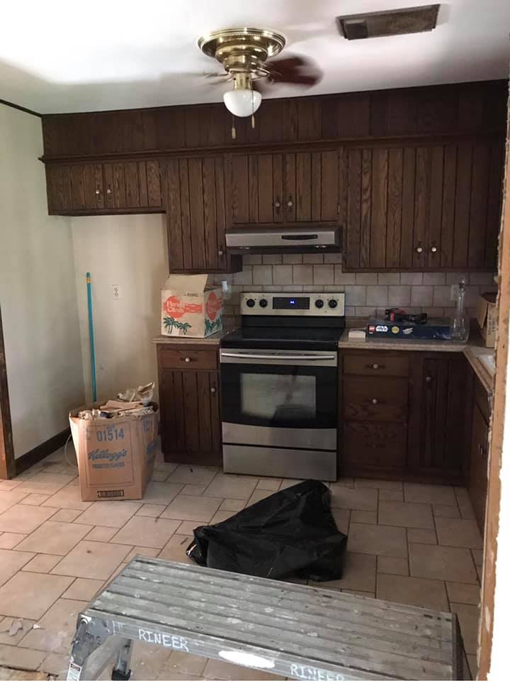 Dim kitchen with dark wood cabinets, stove, tiled floor, and a bench in the foreground.