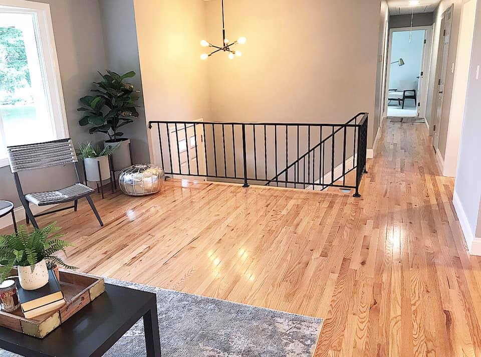 Bright living room with hardwood floors, staircase railing, chandelier, and hallway view