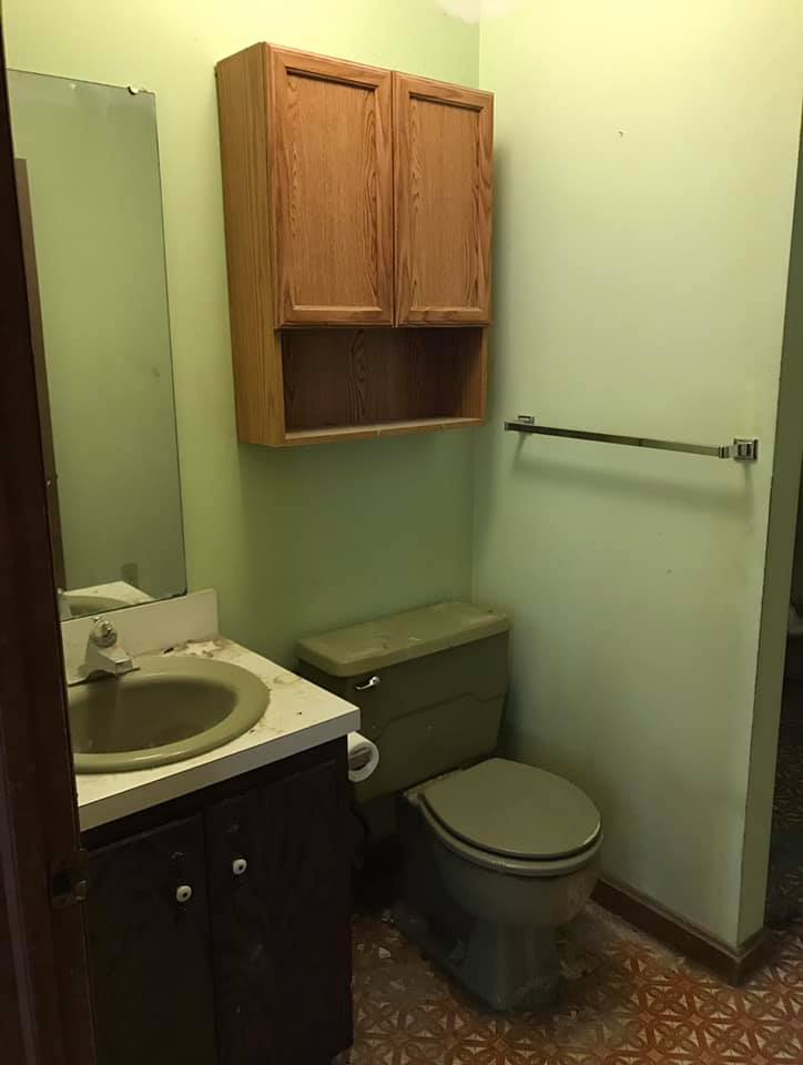 Small bathroom with toilet, sink, mirror, towel bar, and wall cabinet in pale green walls.