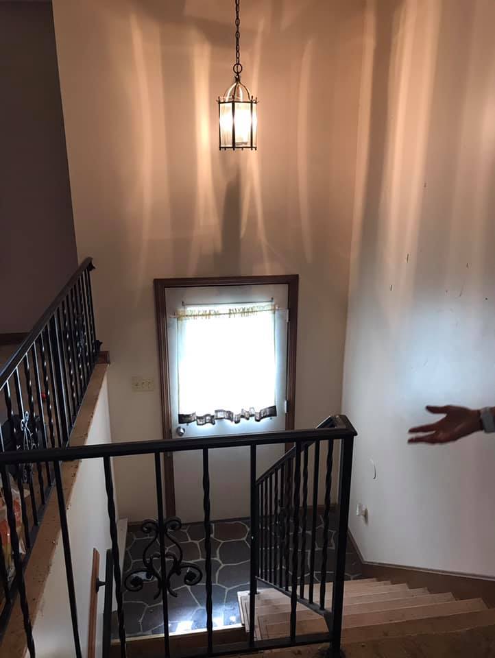 Stairwell with black railings, a hanging lantern, and a bright window; a person’s arm points in from the right.