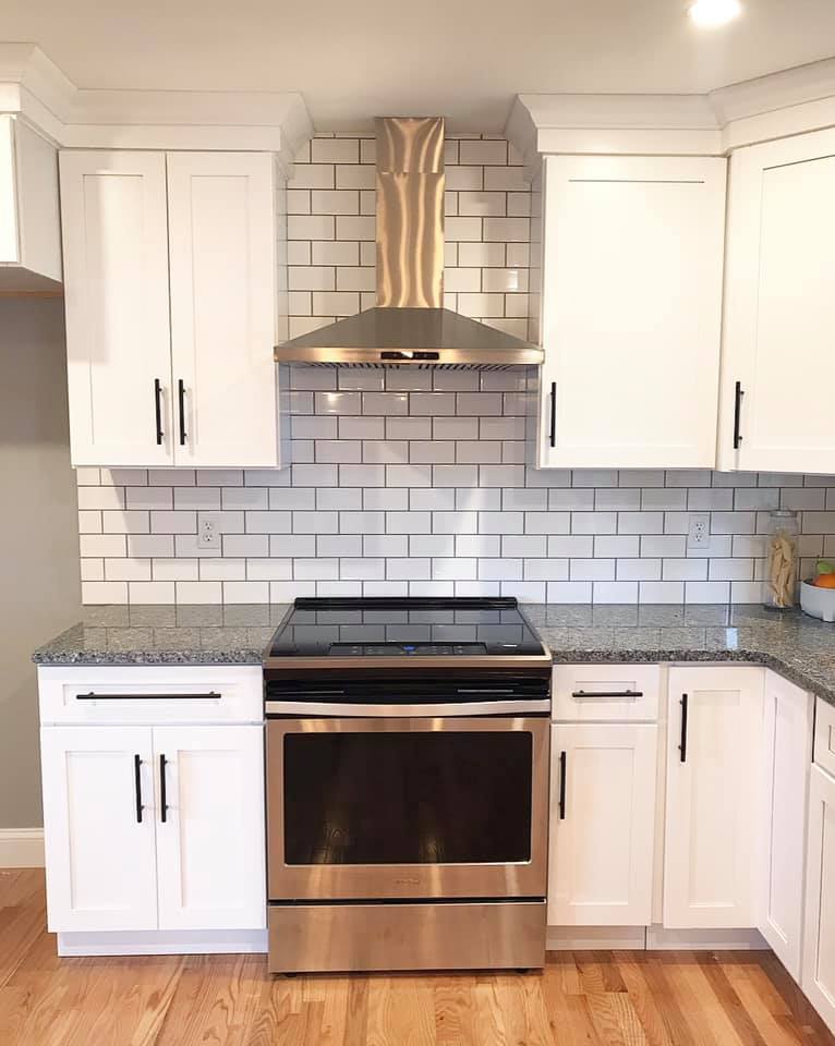Modern white kitchen with stainless steel stove, hood, and subway tile backsplash