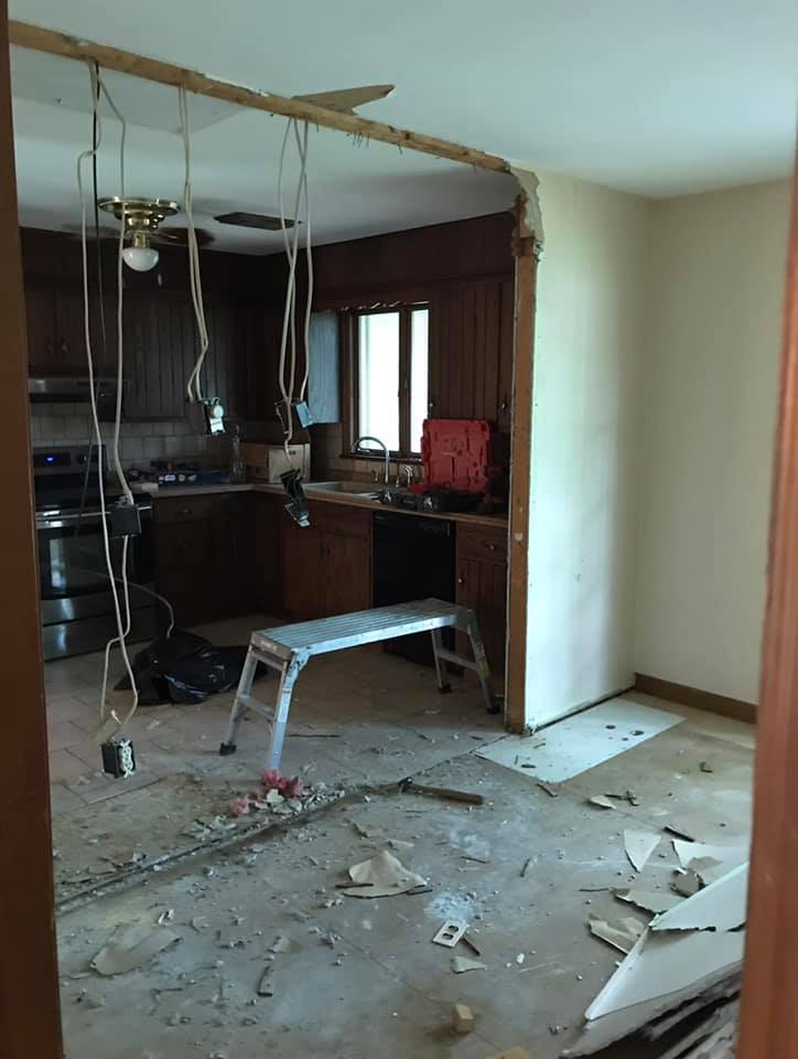 Damaged kitchen under renovation with exposed wires, debris on the floor, and a stepladder.