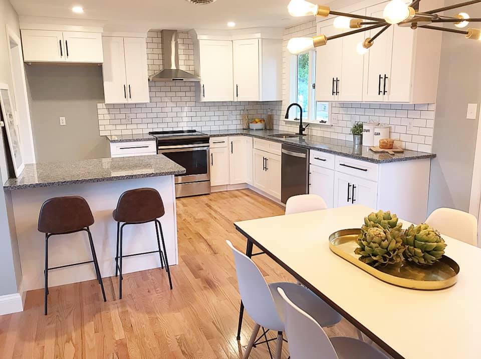 Bright modern kitchen with white cabinets, wood floors, island seating, and a dining table with flowers