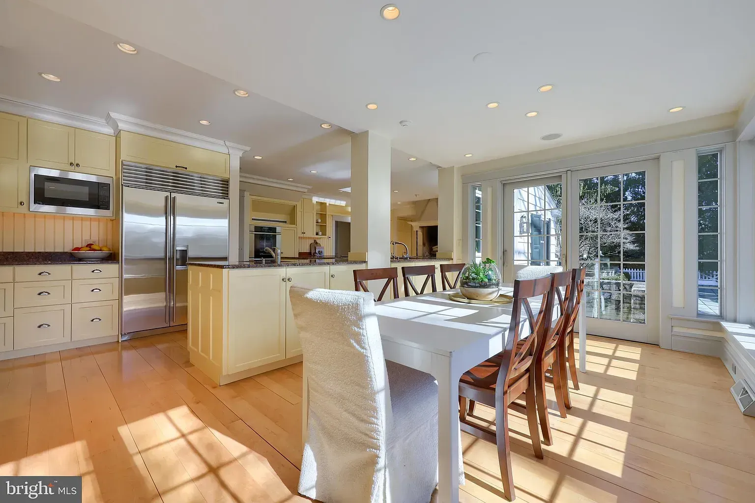 Bright kitchen and dining area with wooden table, white cabinets, and large windows by the garden