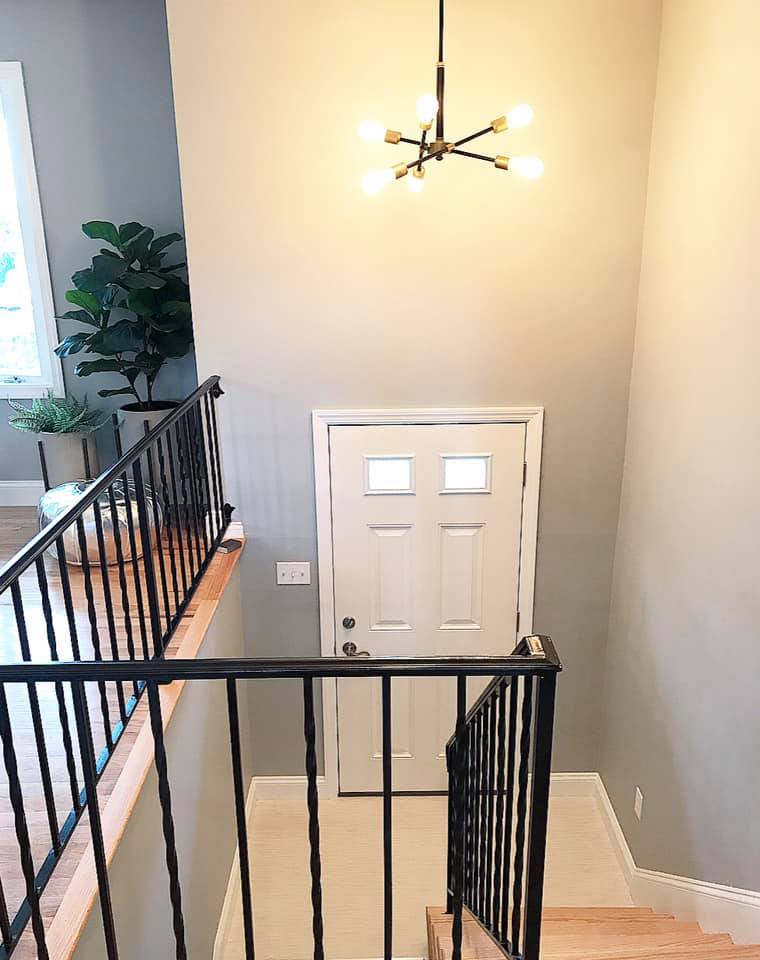 Stair landing with black railings, white front door, gray walls, and a modern ceiling light.