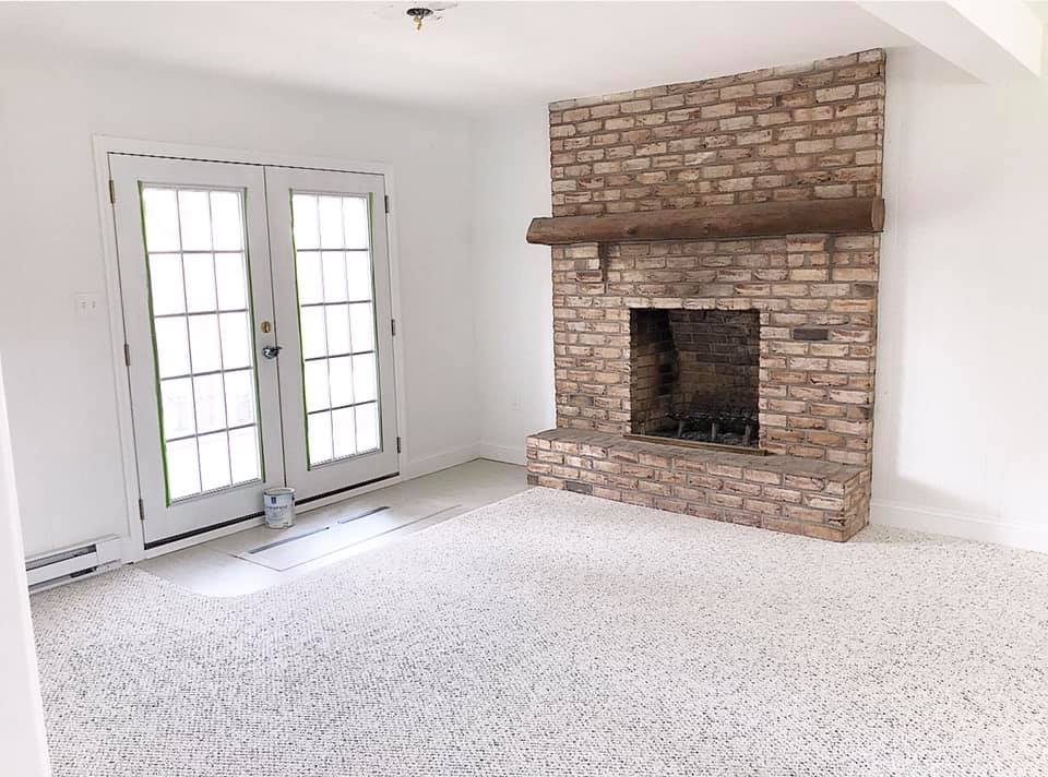 Empty living room with white walls, French doors, and a brick fireplace.