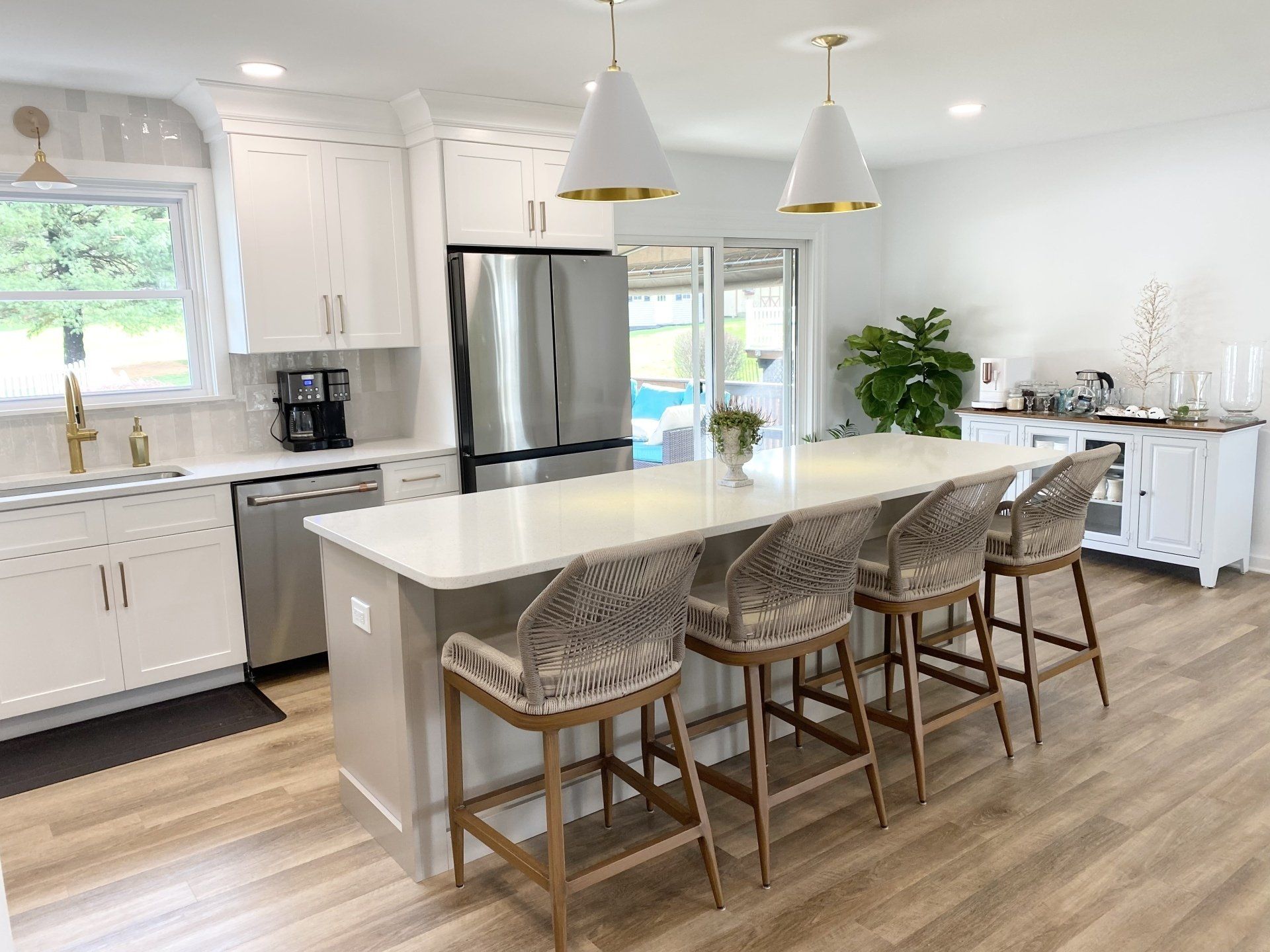 Bright white kitchen with a large island, woven bar stools, stainless steel fridge, and wood floors.