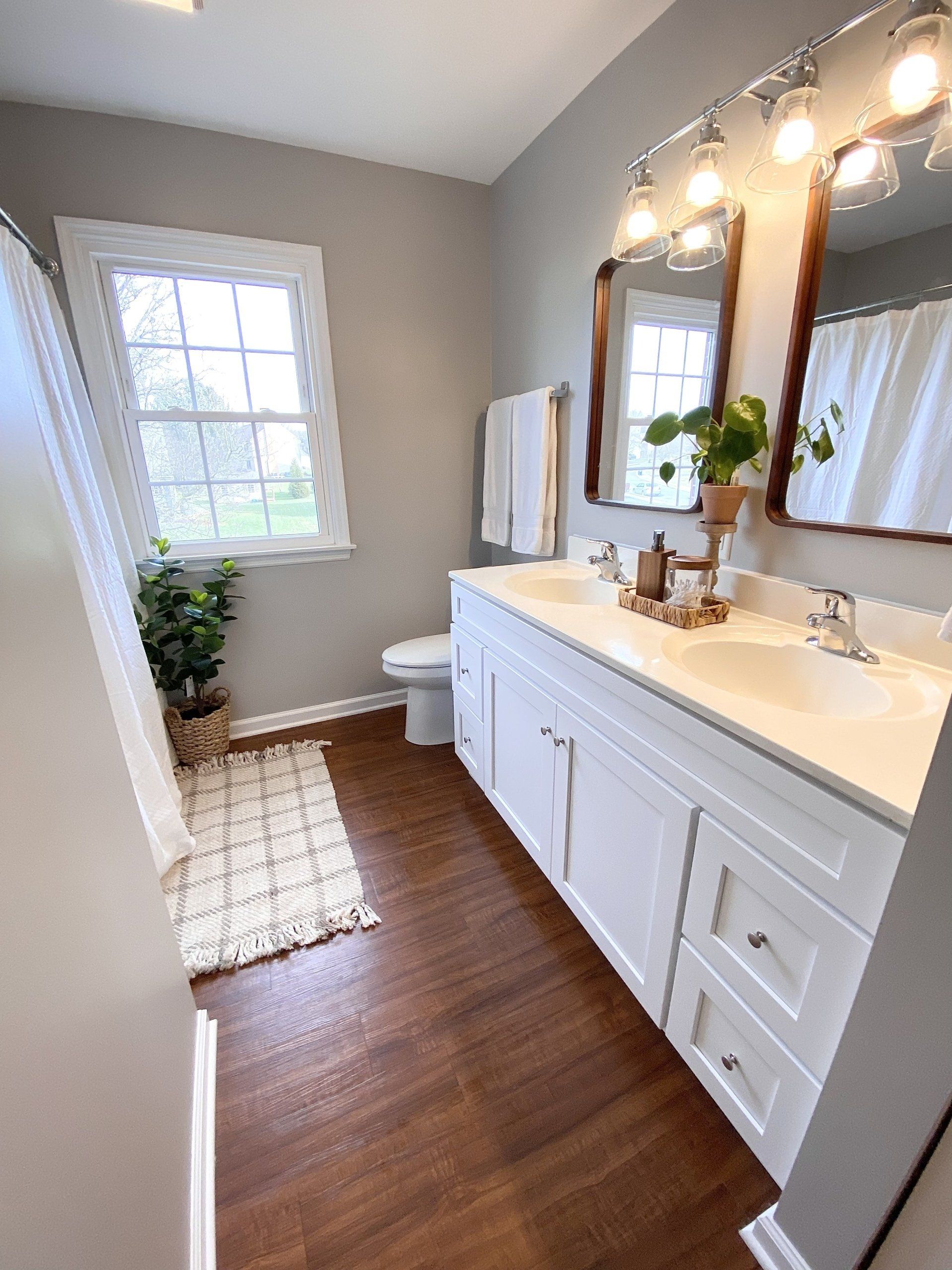 Bright bathroom with double vanity, large mirror, window, and patterned rug.