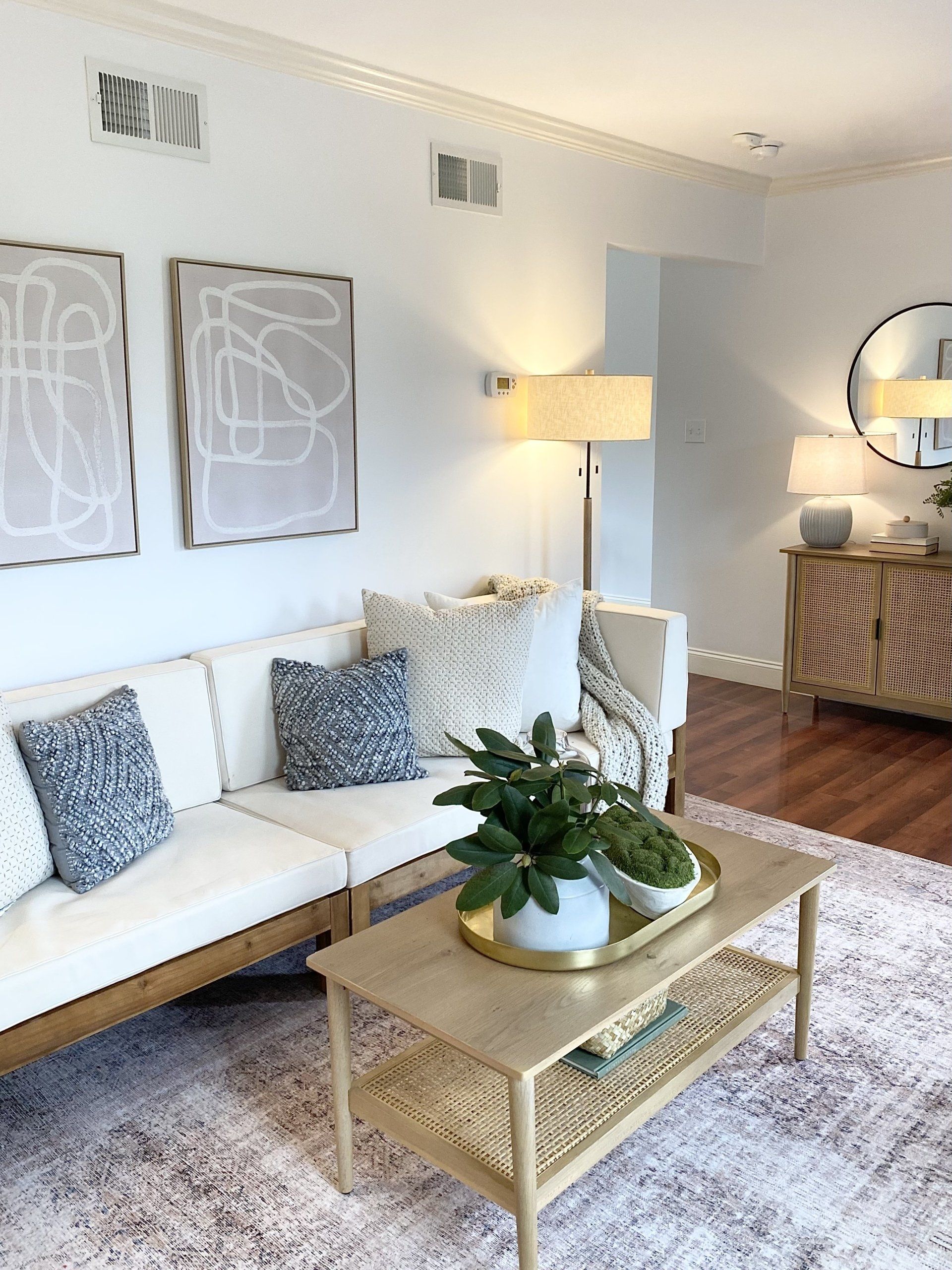 Bright modern living room with white sofa, gold coffee table, floor lamp, and wall art