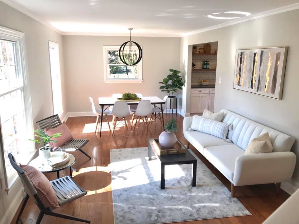 Bright living-dining room with white sofa, chairs, wooden table, rug, and large windows