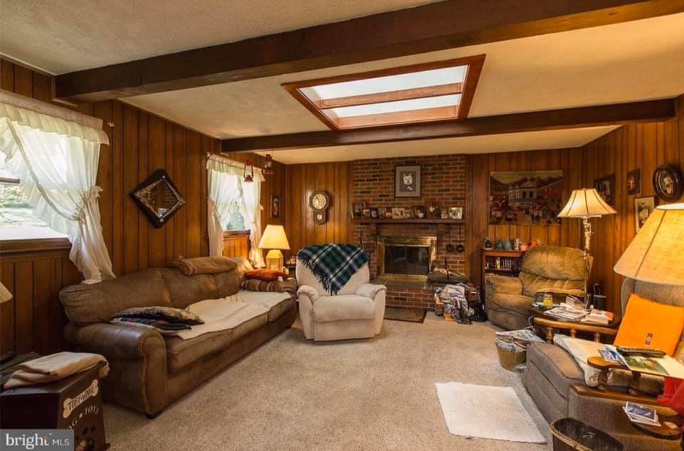 Cozy wood-paneled living room with couch, armchairs, fireplace, and warm lamp lighting