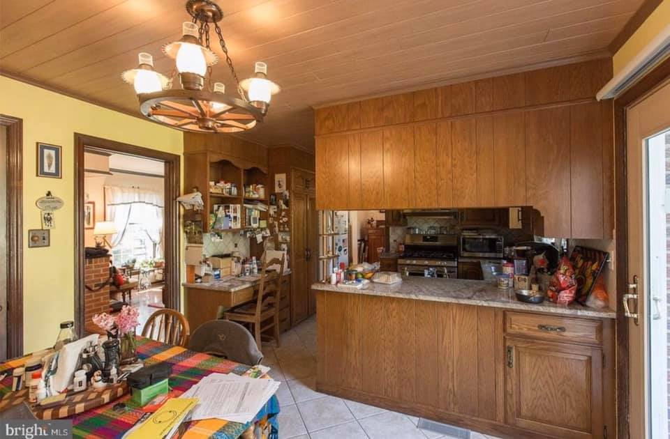 Wood-paneled dining room with chandelier, colorful tablecloth, and open kitchen pass-through