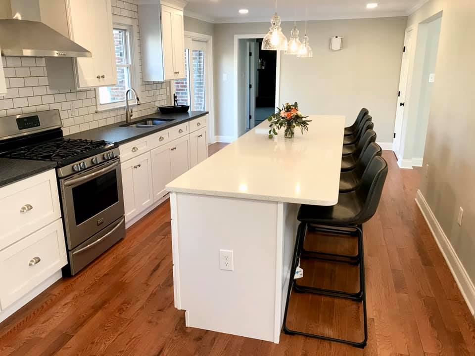 Modern kitchen with white island, black stools, stainless stove, and wood floors