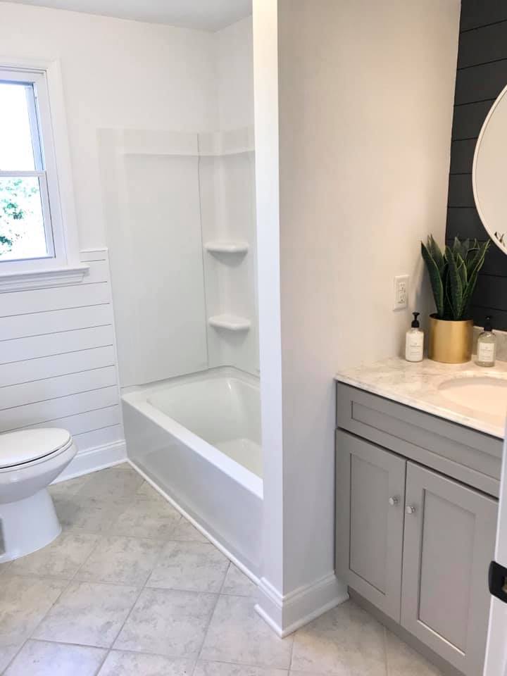 Bright modern bathroom with white tub, toilet, gray tile, and vanity with plant and mirror