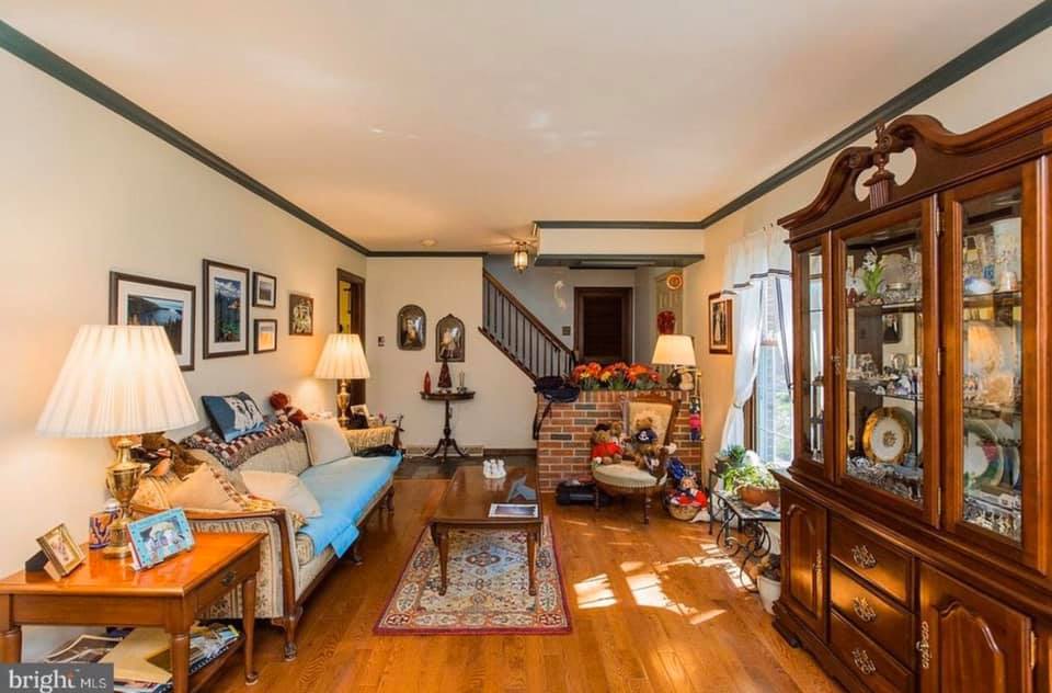 Cozy living room with wood floors, blue sofa, display cabinet, staircase, and sunlight through windows