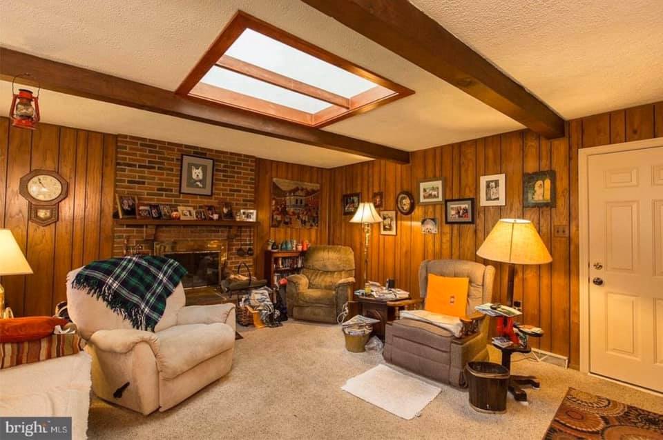 Cozy wood-paneled living room with recliner, fireplace, lamps, framed photos, and skylight ceiling