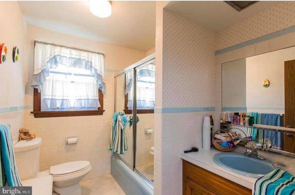 Bright bathroom with blue accents, window above toilet, and sink vanity beside a shower curtain.