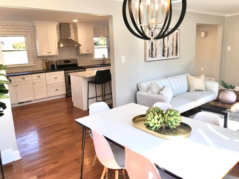 Bright open-plan kitchen and dining room with white furniture, wood floors, and a gray sofa