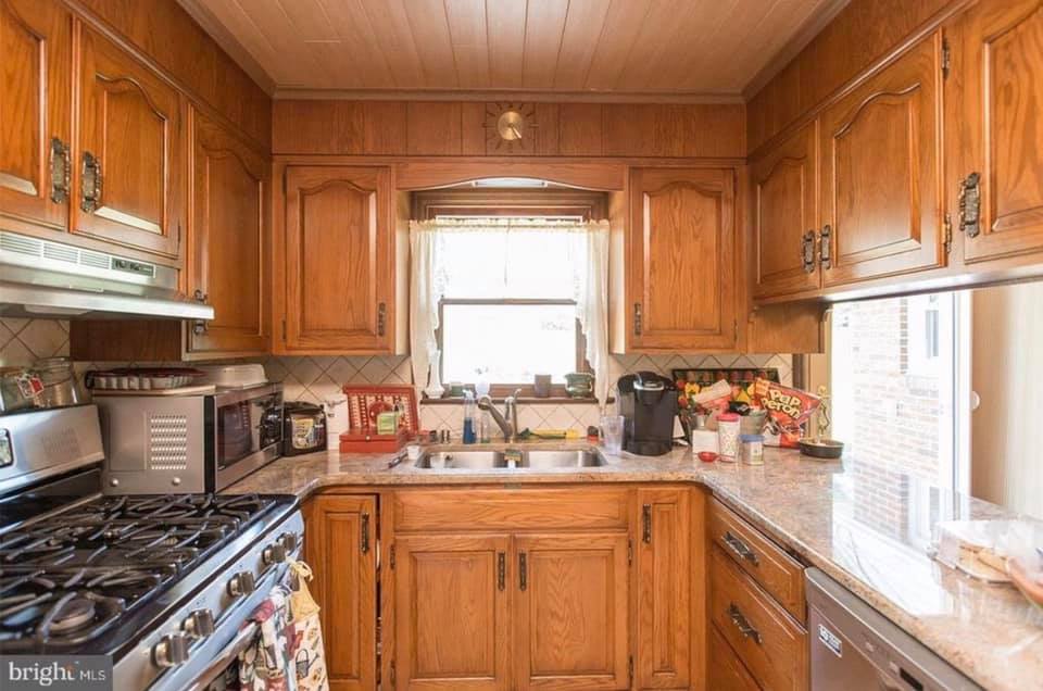 Wooden kitchen with stove, sink, cabinets, and bright window over the sink