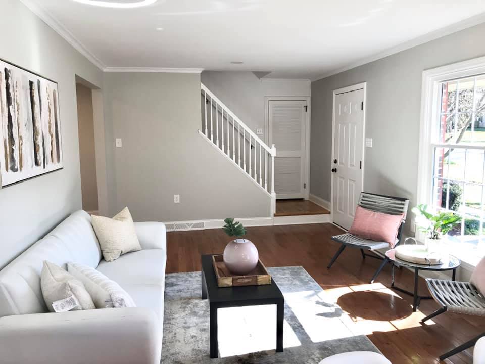 Bright living room with white sofa, black coffee table, pink chair, rug, and staircase in the background