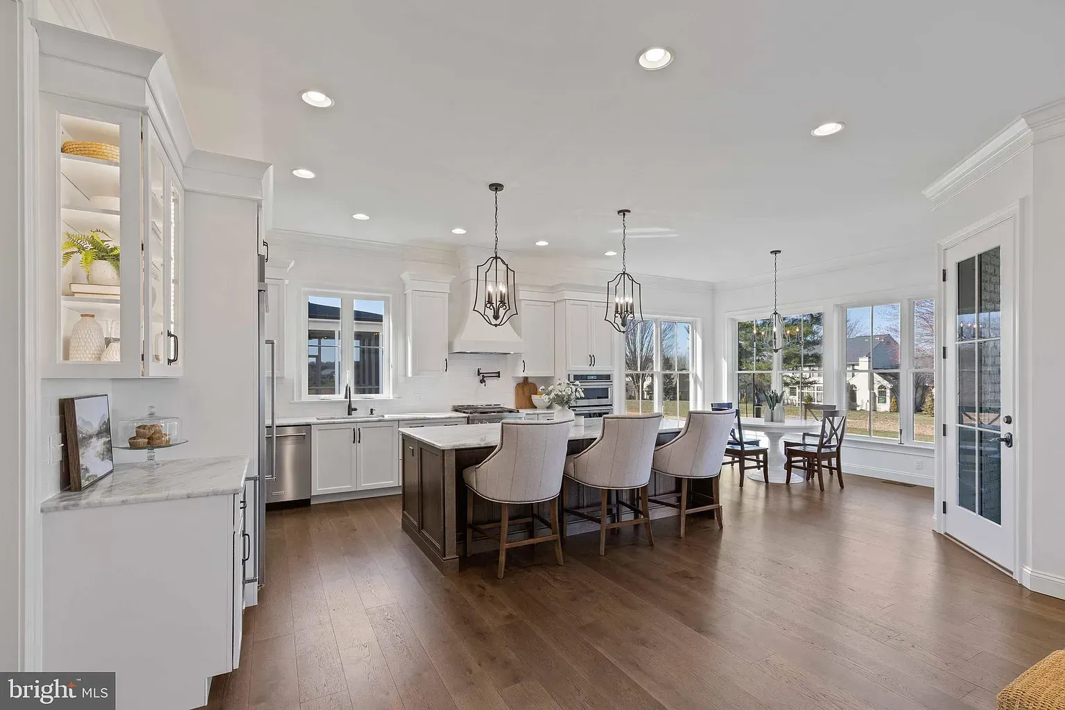 Bright modern kitchen and dining area with white cabinets, island seating, and large windows