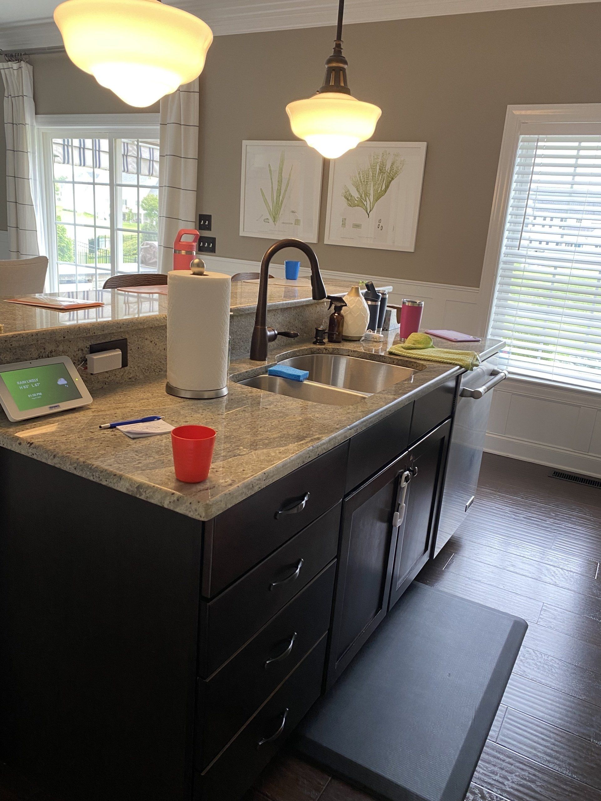 Kitchen island with sink and pendant lights, granite countertop, dark cabinets, and a red cup on the counter.