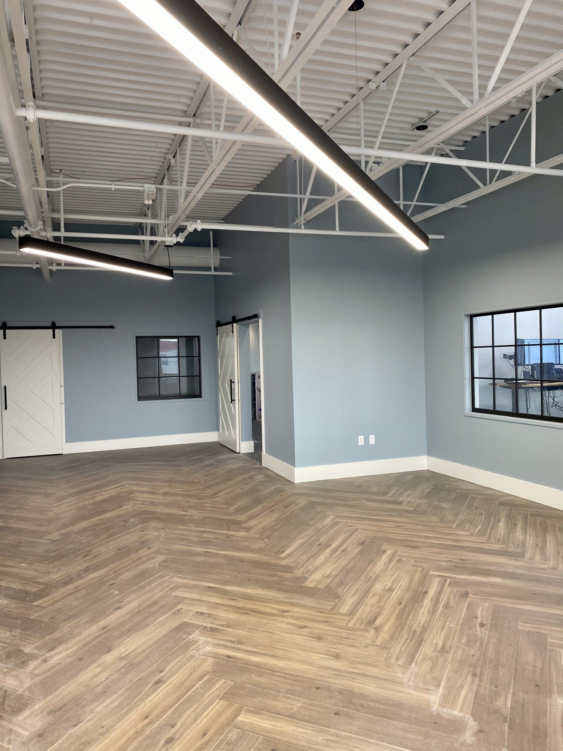 Empty modern office space with blue walls, herringbone wood floor, windows, and exposed ceiling beams