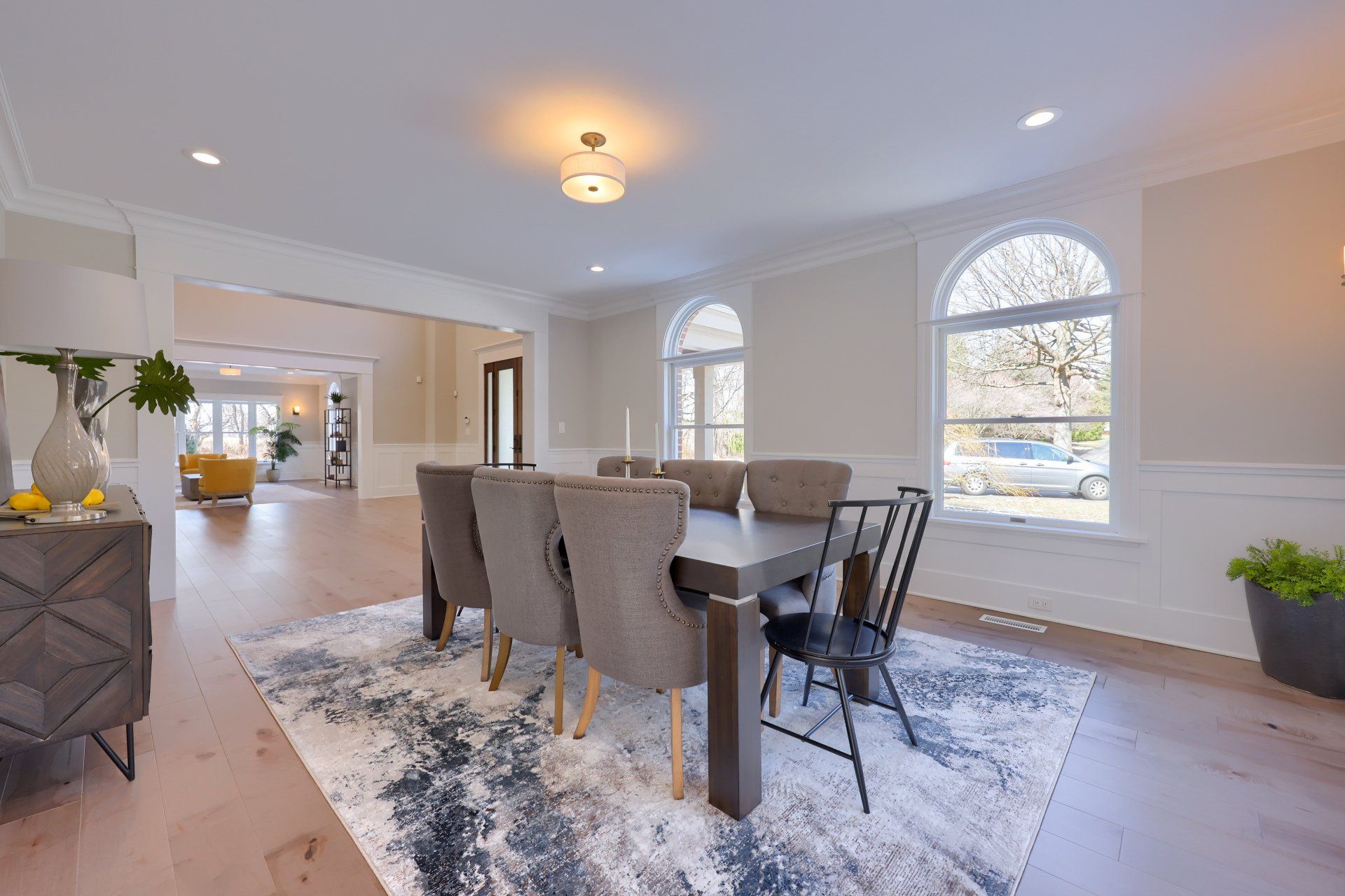 Elegant dining room with gray chairs, wood table, patterned rug, and large arched windows
