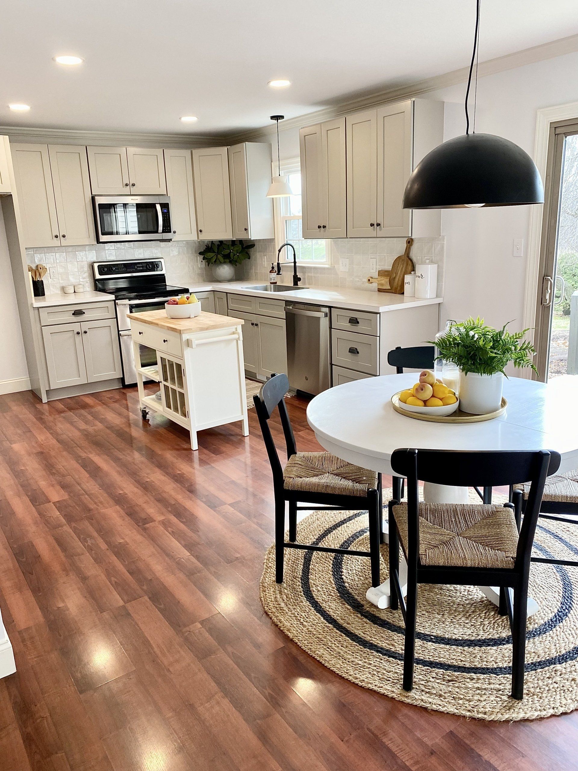 Bright kitchen and dining area with white cabinets, wood floors, and a small round table on a rug.