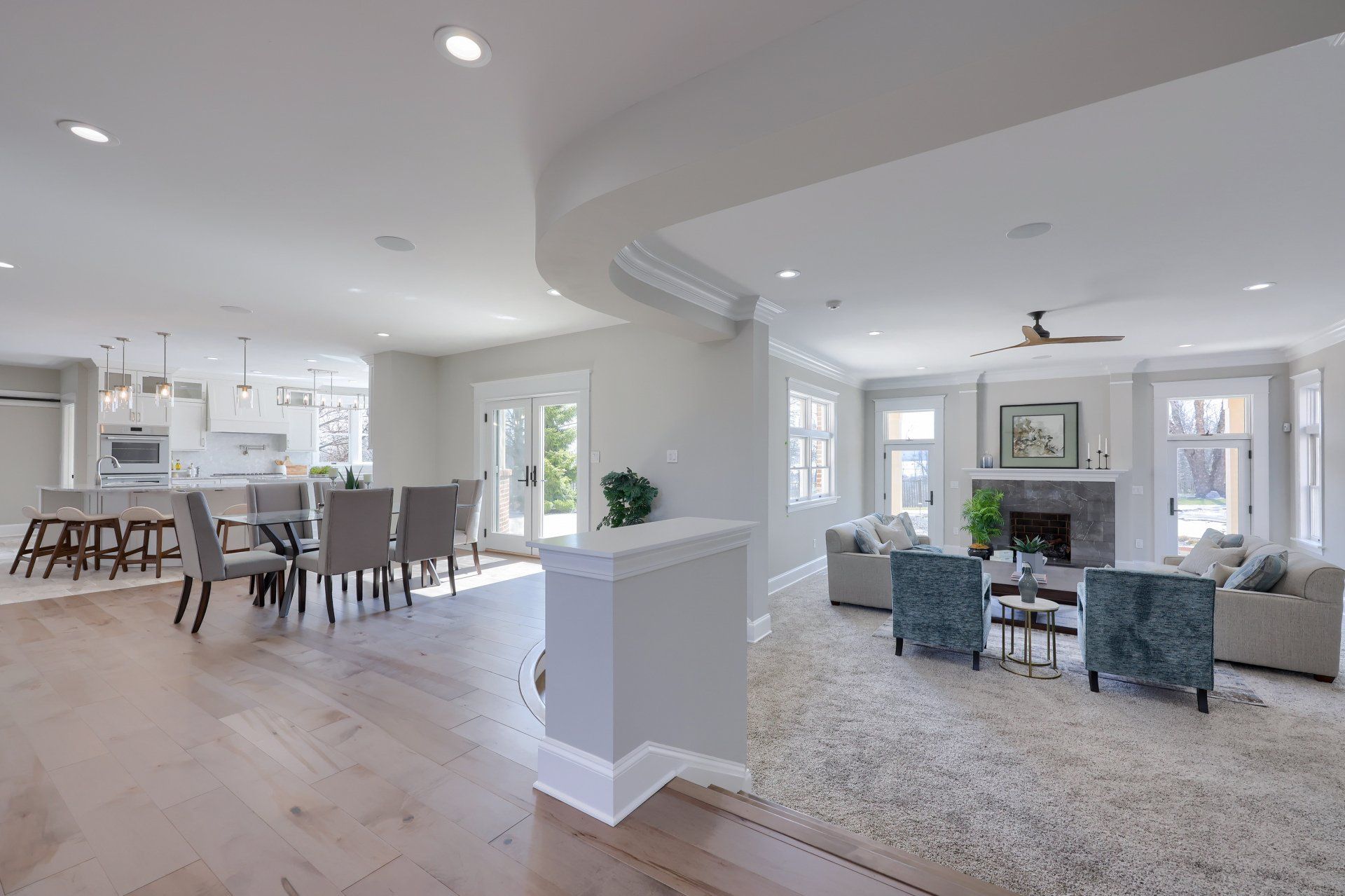 Open-concept living room and kitchen with white walls, light wood floors, and gray seating around a fireplace.