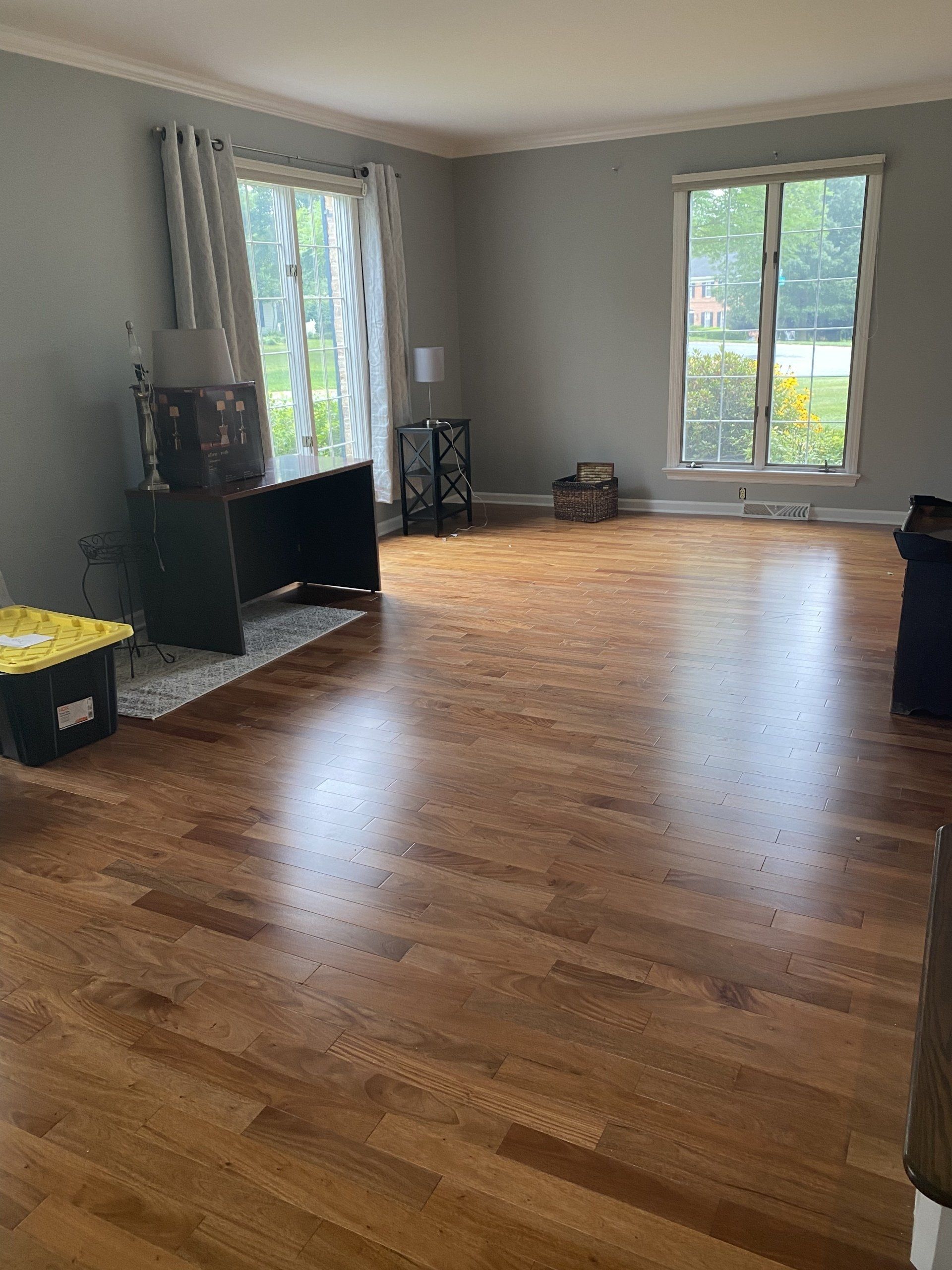 Spacious empty living room with hardwood floors, large windows, and a black cabinet near the wall