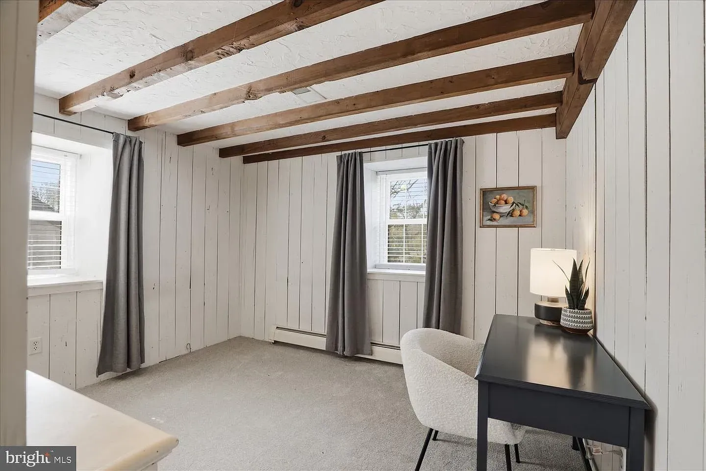 Bright bedroom with exposed wooden beams, white walls, gray curtains, and a black desk by the window.