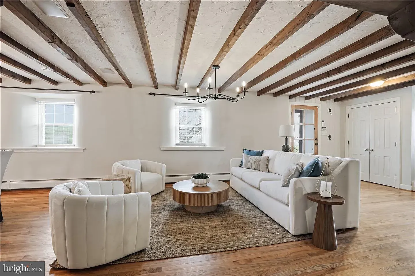 Bright living room with exposed wood beams, white furniture, a rug, and hardwood floors