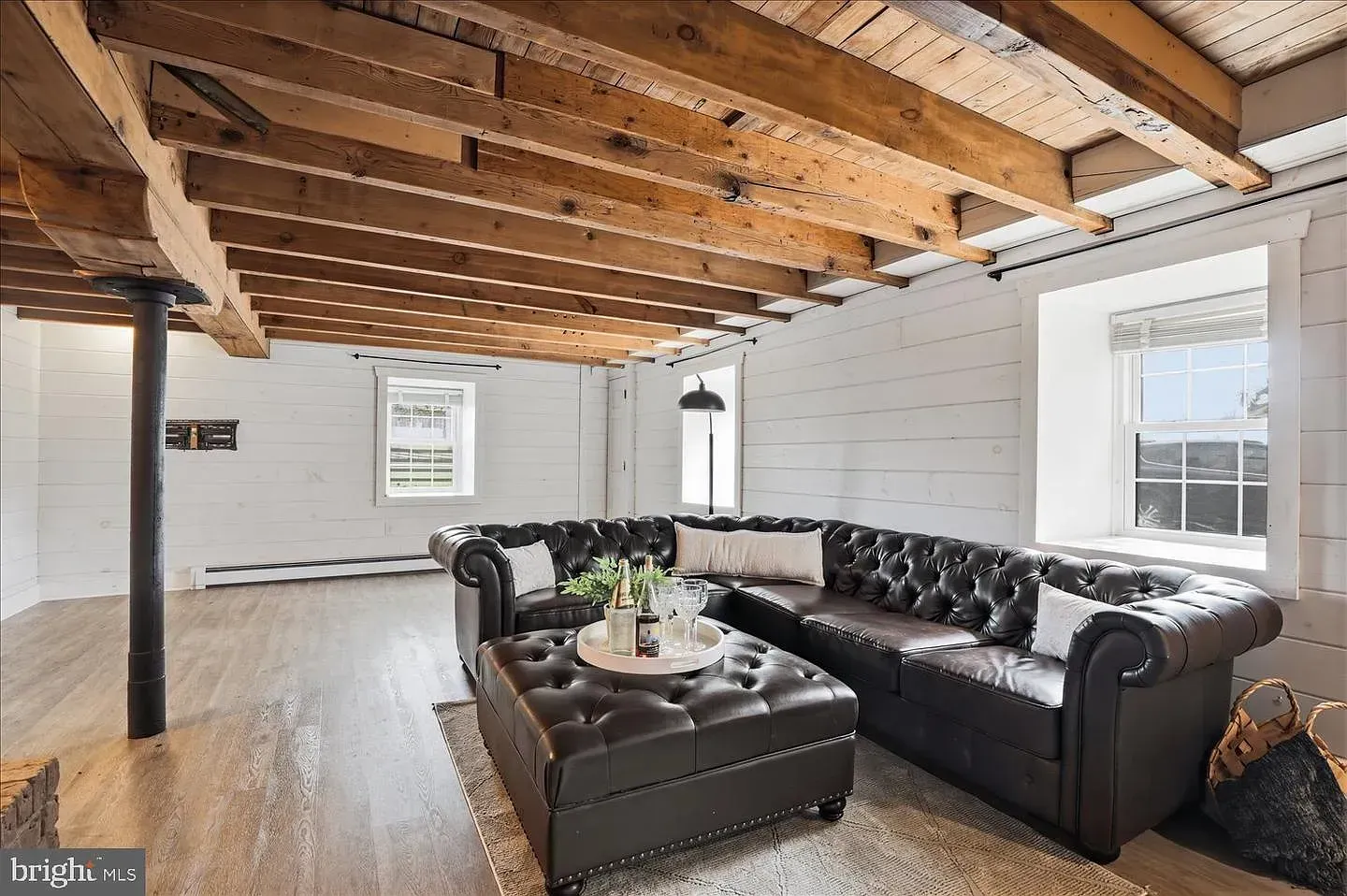 Bright living room with exposed wood beams, white walls, and dark leather sectional sofa.