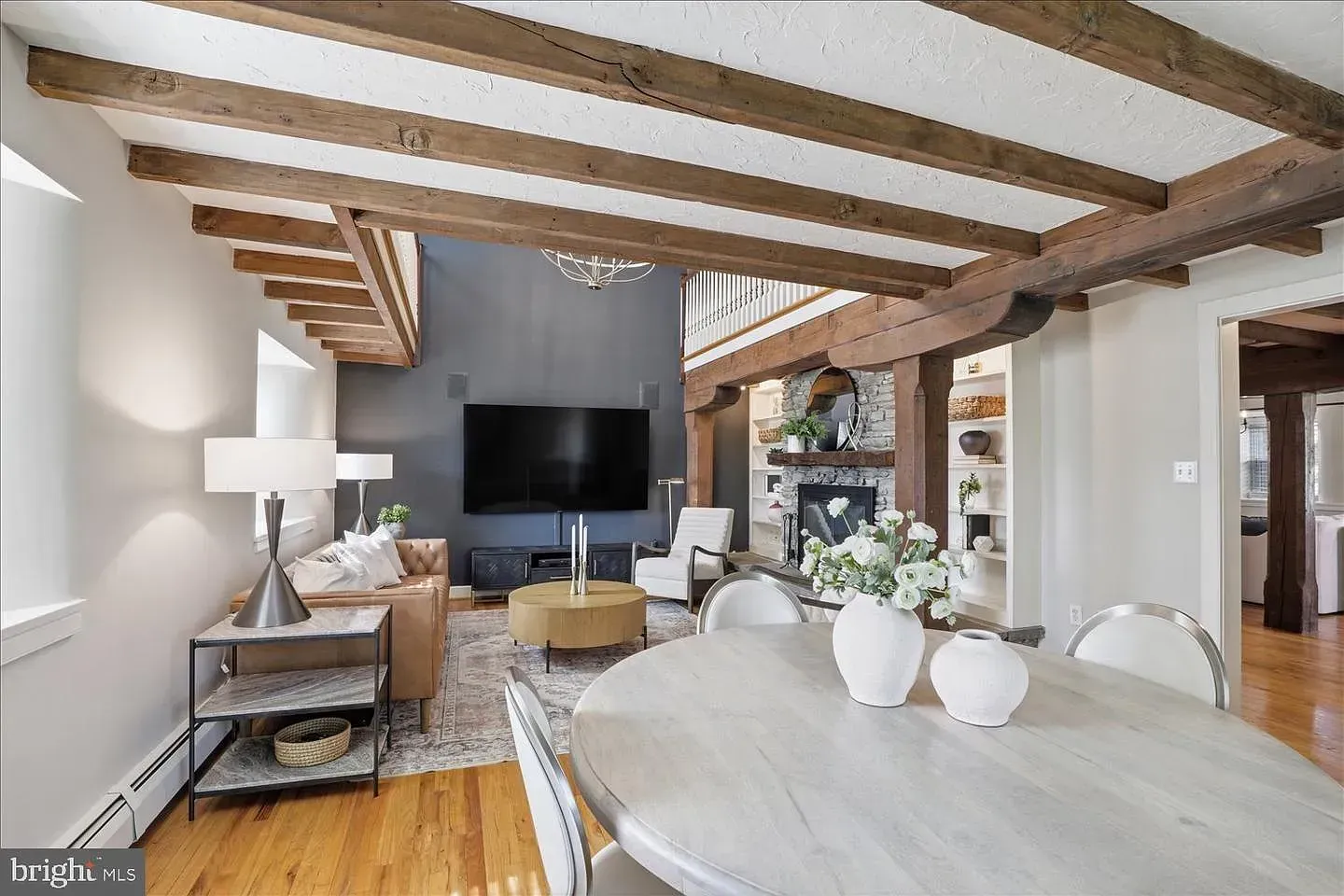 Bright living room with exposed wood beams, TV, and dining table near large windows