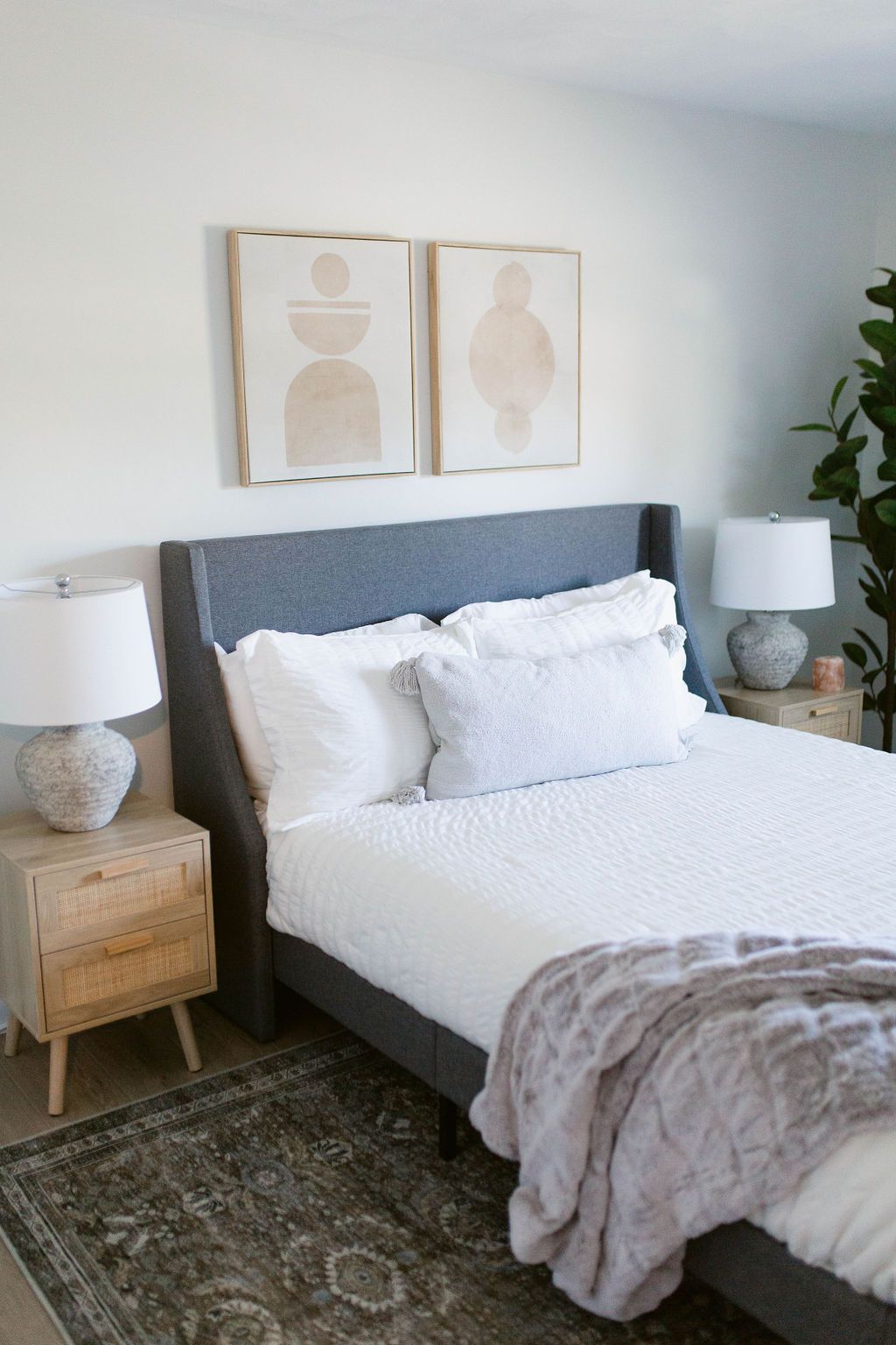 Cozy bedroom with gray upholstered bed, white bedding, bedside lamps, and minimalist wall art