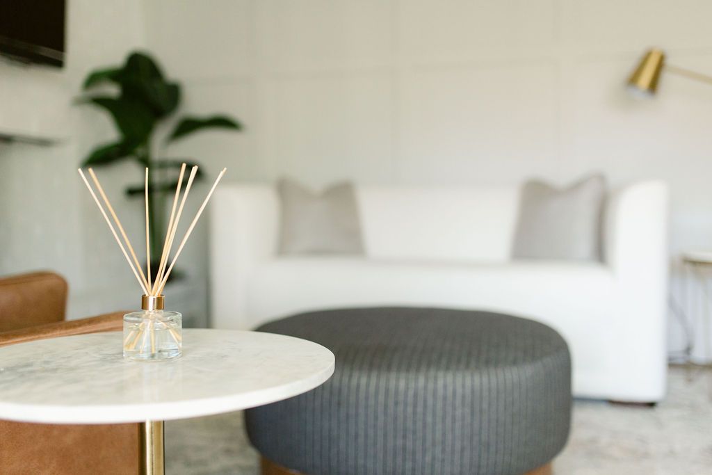 Modern living room with a white sofa, gray ottoman, round table, and reed diffuser