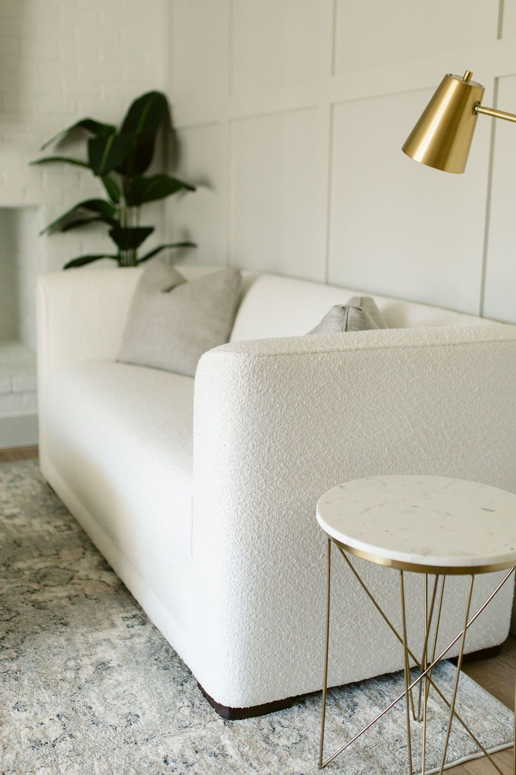 Minimalist white living room with a sofa, gold lamp, side table, and potted plant