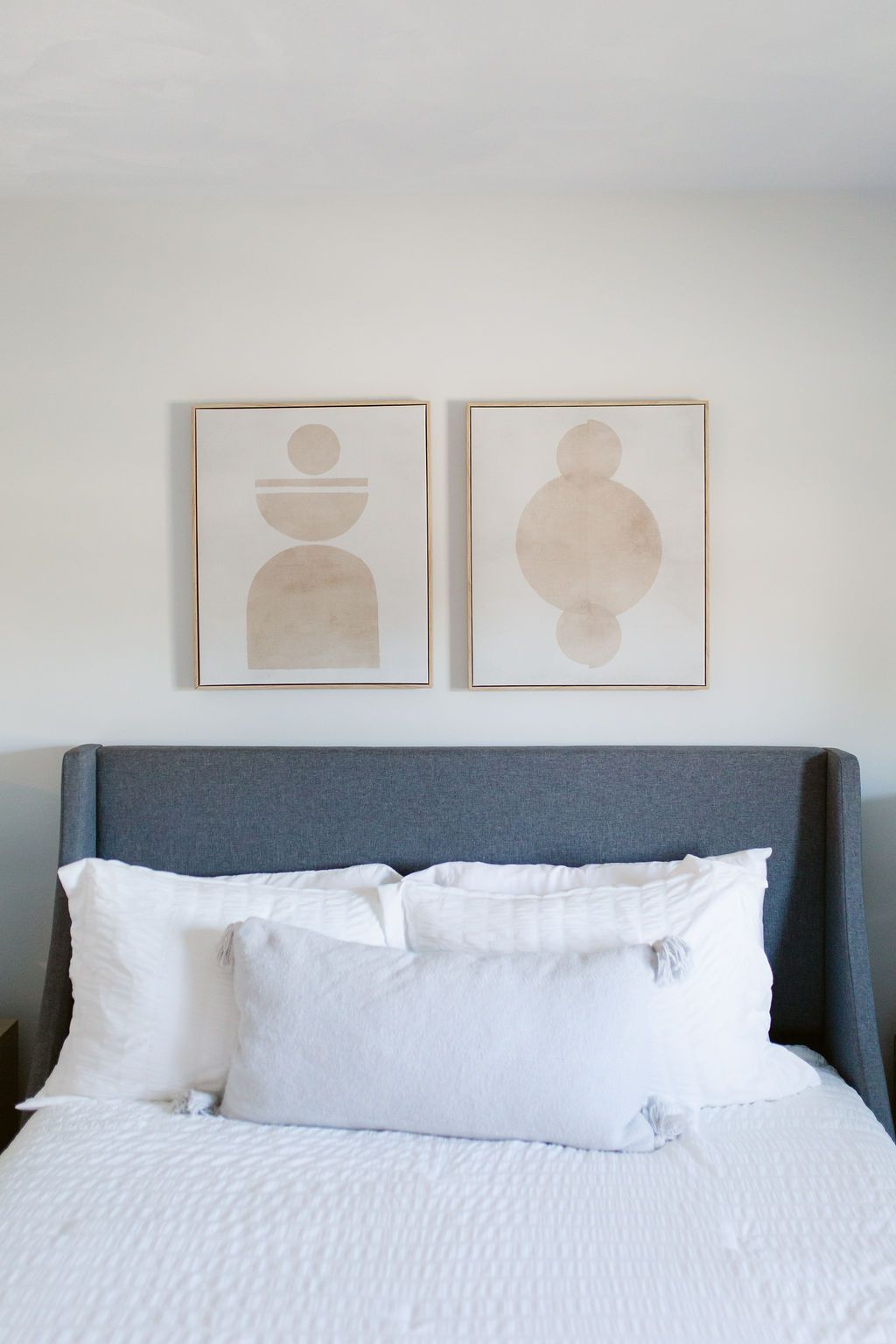 Minimal bedroom with blue upholstered headboard, white bedding, and two framed abstract prints above the bed