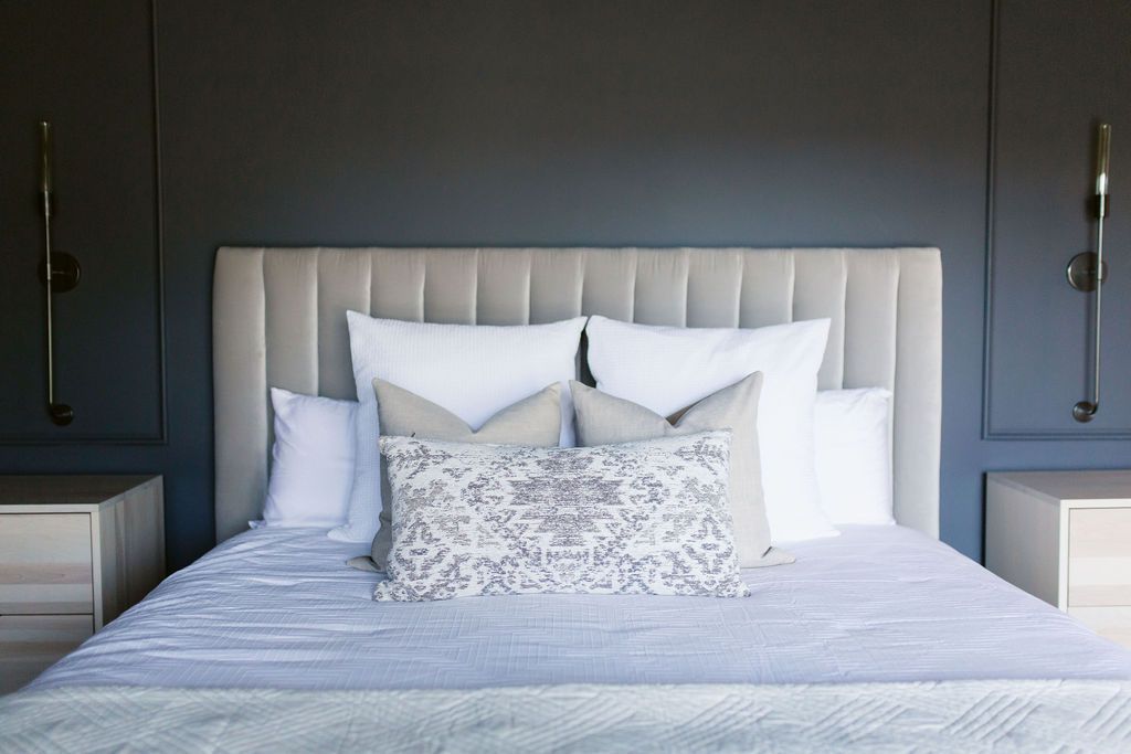 Modern bedroom with a white upholstered bed, layered pillows, and dark gray walls