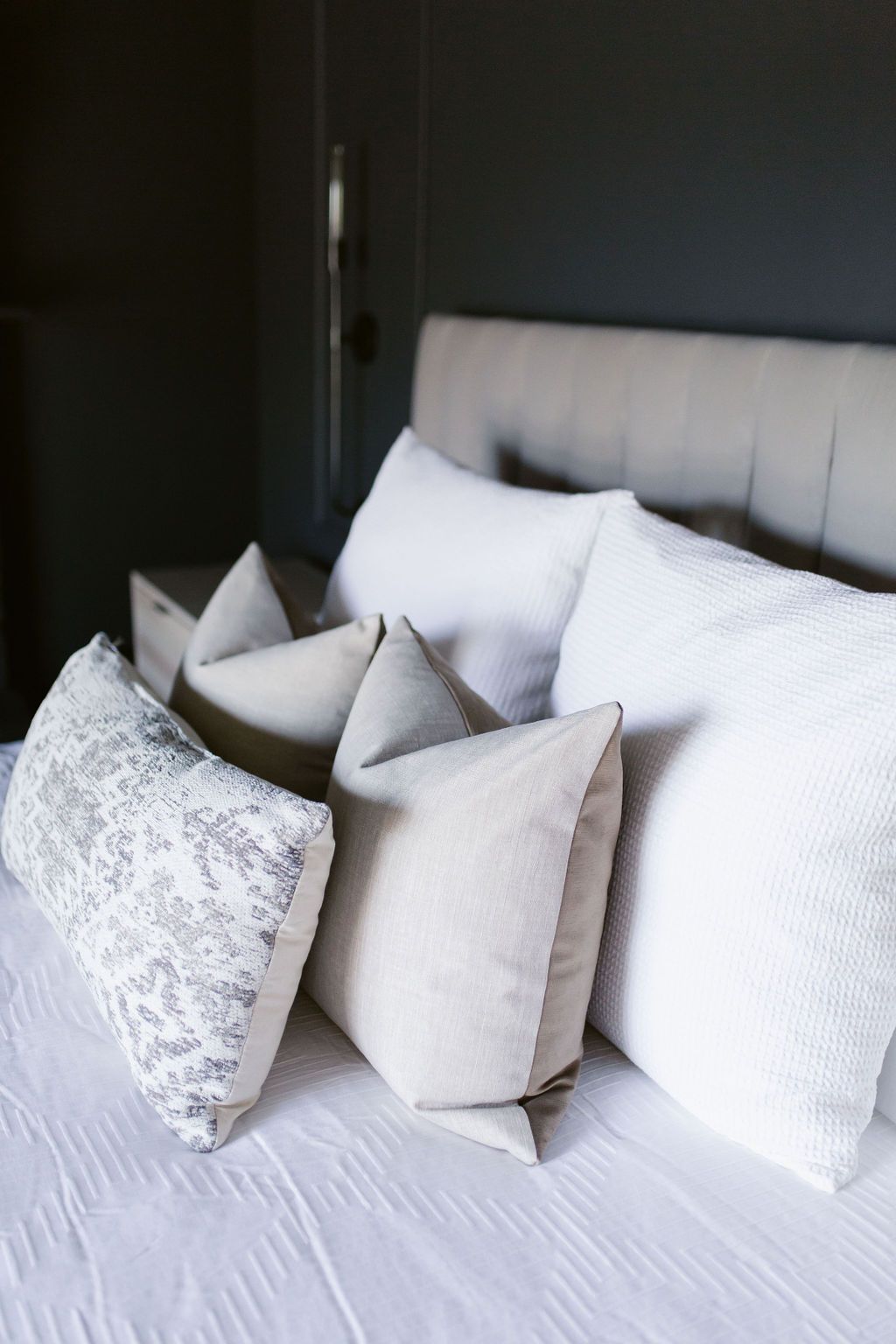 White bed with layered pillows against a dark wall in a modern bedroom