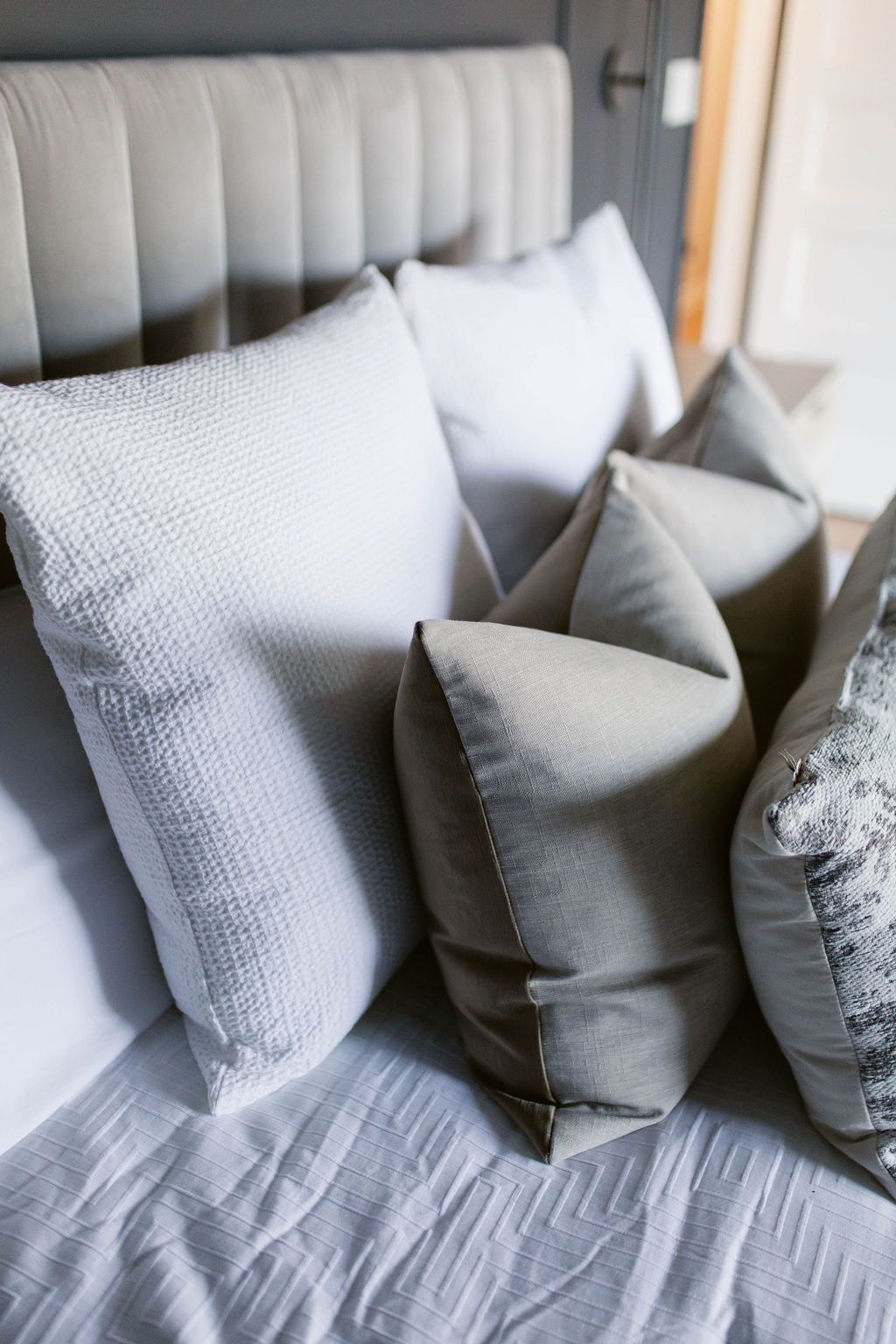 Gray and white pillows on a neatly made bed with a tufted headboard