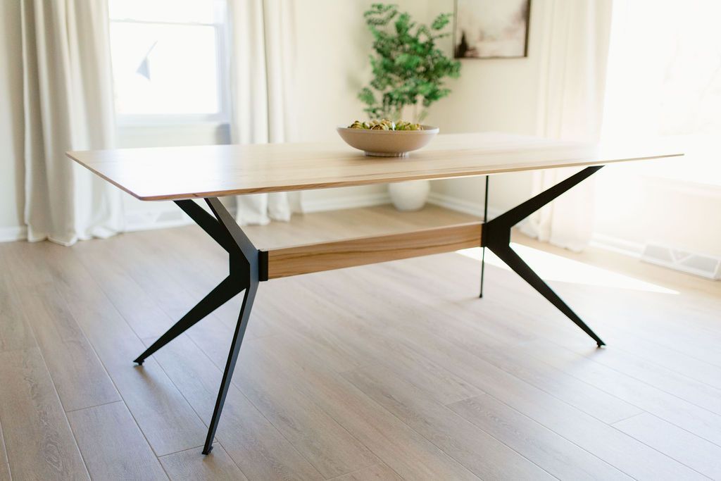Modern dining table with black metal legs in a bright room with curtains and a plant centerpiece