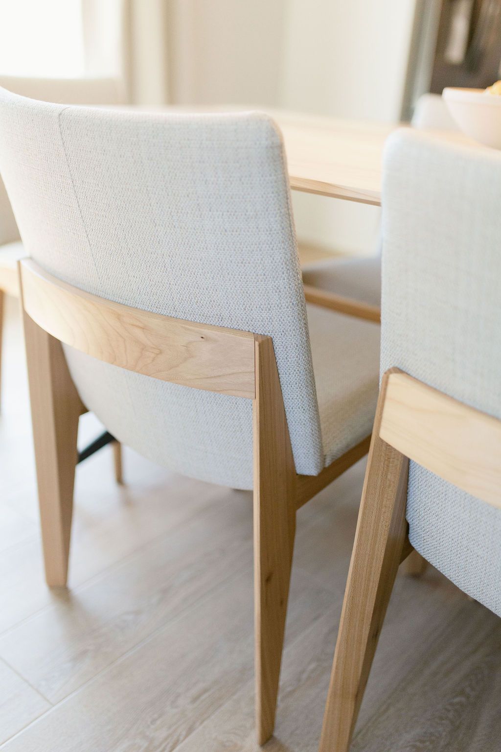 Two light upholstered dining chairs with wooden frames on a bright floor