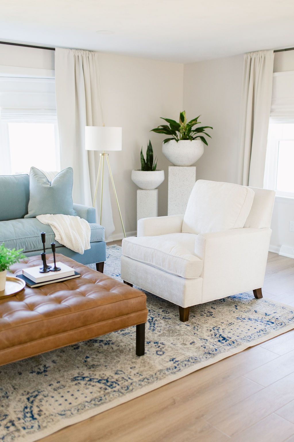 Bright living room with white armchair, blue sofa, tan ottoman, and potted plants on a patterned rug